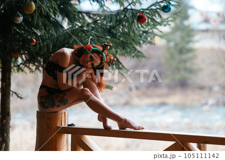 Beautiful girl in bikini sitting against of snow-covered trees in winter Beautiful girl in bikini sitting against of snow-covered trees in winter 105111142