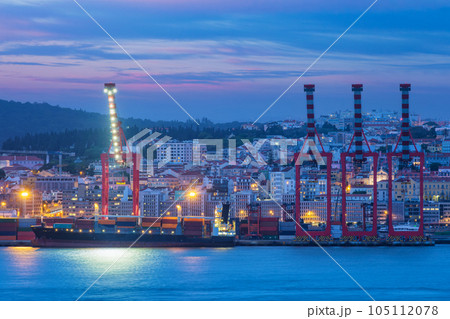 View of Lisbon port with moored sea container ship with port cranes in the evening twilight over Tagus river. Lisbon, Portugal 105112078