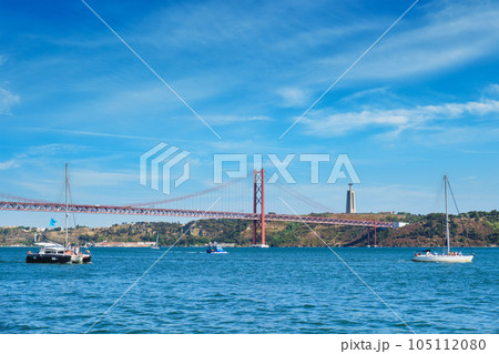 View of 25 de Abril Bridge famous tourist landmark over Tagus river, Christ the King monument and a tourist yacht boat. Lisbon, Portugal 105112080