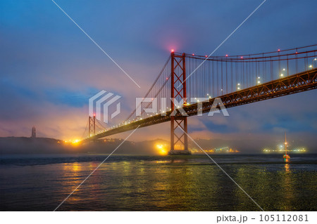 View of 25 de Abril Bridge famous tourist landmark of Lisbon connecting Lisboa and Almada in heavy fog mist wtih yacht boats passing under. Lisbon, Portugal View of 25 de Abril Bridge famous tourist landmark of Lisbon connecting Lisboa and Almada in heavy fog mist wtih yacht boats passing under. Lisbon, Portugal 105112081