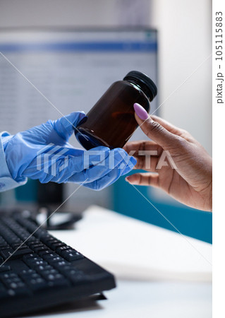 Doctor offering medicine pill bottle to patient during appointment. Clinical consultation by doctor with protective medical gloves prescribing medicine inside hospital office, closeup 105115883