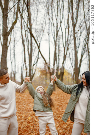 Man, woman and their little girl standing in autumn forest and laughing. Brunette woman and man play with daughter. Family wearing beige sportive costumes. Man, woman and their little girl standing in autumn forest and laughing. Brunette woman and man play with daughter. Family wearing beige sportive costumes. 105117862