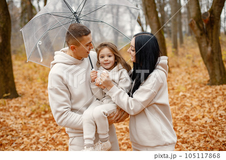 Man, woman and their little girl standing in autumn forest and laughing. Brunette woman and man holding their daughter on hands. Family wearing beige sportive costumes. Man, woman and their little girl standing in autumn forest and laughing. Brunette woman and man holding their daughter on hands. Family wearing beige sportive costumes. 105117868