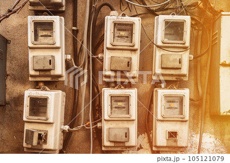 Various Electric Meters Stand A Row. Energy Consumption Concept. Impact On Environment. Dial Electric Power Meters Measuring Power Usage. Need For Saving Energy. Electricity Meter Measures Current 105121079