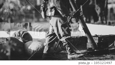 Close-up View On Re-enactor Dressed As German Wehrmacht Infantry Soldier In World War Ii With Submachine Gun Mp 40 Patrols Territory Of Mortar Crew. German Soldier Guards Mortar. Black And White 105121497