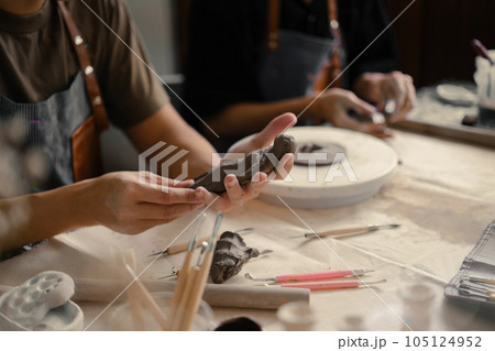 Craftspeople wearing aprons working with raw clay, shaping and decorating pottery in workshop Craftspeople wearing aprons working with raw clay, shaping and decorating pottery in workshop 105124952