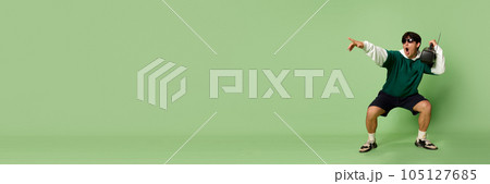 Portrait of young stylish man in sunglasses and sport style clothes listening to music in retro player against green studio background 105127685