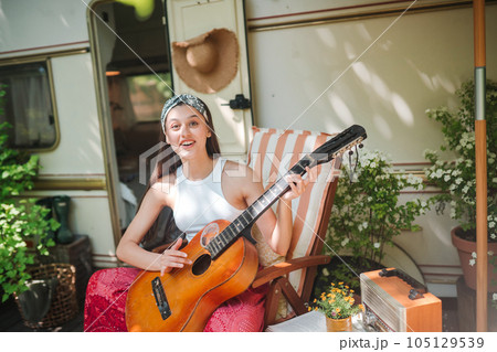 Happy hippie girl is having a good time with playing on guitar in camper trailer. Holiday, vacation, trip concept. 105129539