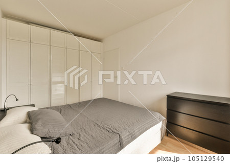 a bedroom with a bed, dresser and mirror on the wall in front of the room is white shutters 105129540