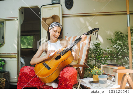 Happy hippie girl is having a good time with playing on guitar in camper trailer. Holiday, vacation, trip concept. Happy hippie girl is having a good time with playing on guitar in camper trailer. Holiday, vacation, trip concept. 105129543