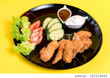 Chicken nuggets with cucumber, tomatoes and lettuce on a black plate, chicken nuggets on a yellow background. Chicken nuggets with cucumber, tomatoes and lettuce on a black plate, chicken nuggets on a yellow background. 105129849