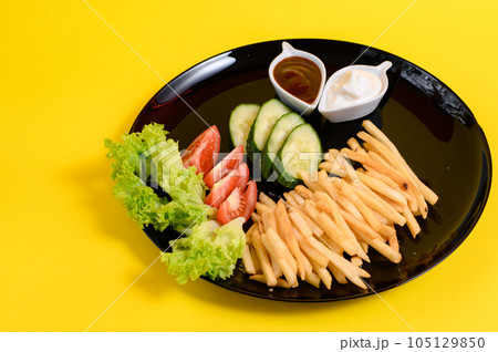 Plate of french fries with lettuce, tomatoes and cucumbers, sauces in white french fries plates. Plate of french fries with lettuce, tomatoes and cucumbers, sauces in white french fries plates. 105129850