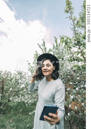 beautiful Asian girl in a hat takes a selfie on a smartphone in a blooming garden 105134721