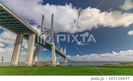 Vasco da Gama bridge timelapse hyperlapse with green lawn on a waterfront and blue cloudy sky. Lisbon, Portugal. Vasco da Gama bridge timelapse hyperlapse with green lawn on a waterfront and blue cloudy sky. Lisbon, Portugal. 105136647