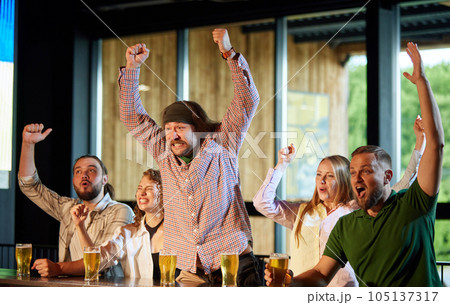 Happy and excited young men and women, friends meeting at pub, bar, watching online sport match translation and cheering up favourite team 105137317