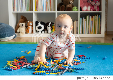 A one-year-old baby sits on the carpet and plays with a designer at home. A one-year-old baby sits on the carpet and plays with a designer at home. 105137772