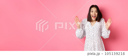 Happy and surprised asian girl receive surprise, looking glad hearing good news, standing amazed in dress against pink background Happy and surprised asian girl receive surprise, looking glad hearing good news, standing amazed in dress against pink background 105139218