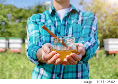 A shows a jar of honey against the background of a bee apiary. 105140362