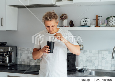 Young man eating a ready dehydrated meal out of portion pot with background of bag with balanced nutritionally complete meals on kitchen table. Food replacement, plant-based protein. Biohacking. Young man eating a ready dehydrated meal out of portion pot with background of bag with balanced nutritionally complete meals on kitchen table. Food replacement, plant-based protein. Biohacking. 105140460