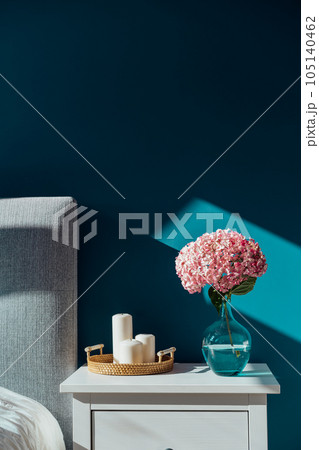 Stylish modern cosy bedroom in dark colors. Cozy interior with turquoise walls, home decor. Bed with grey fabric headboard, white blanket, bedside table, vase with hydrangea flower, candles. Vertical. Stylish modern cosy bedroom in dark colors. Cozy interior with turquoise walls, home decor. Bed with grey fabric headboard, white blanket, bedside table, vase with hydrangea flower, candles. Vertical. 105140462