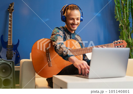 Young man sitting in his room and watching guitar tutorial on laptop 105140801