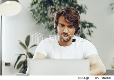 Young man businessman with headset working on laptop from home Young man businessman with headset working on laptop from home 105140866