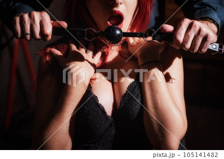 A man dominates and puts a gag in his partner mouth. BDSM concept. Portrait of a woman in seductive underwear with an intimate toy in her mouth. Sexy couple plays love games. 105141482