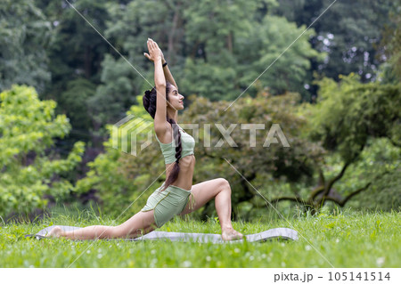 Young beautiful woman in the park on a sports mat doing fitness and doing active sports exercises, Hindu woman doing yoga in the park in the morning among the trees, stretching and meditating. 105141514