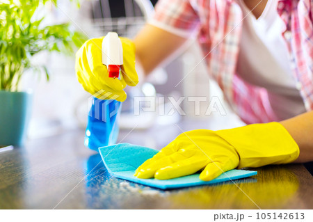 Housewife in yellow gloves wipes dust using spray detergent and rag 105142613