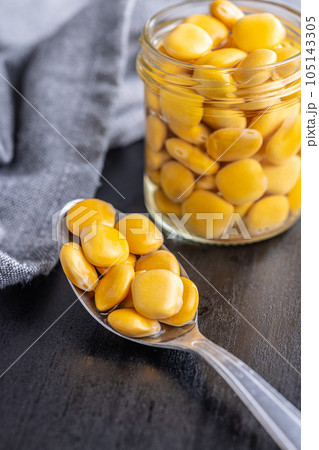 Lupini beans in brine. Pickled lupin in spoon on black table. 105143305