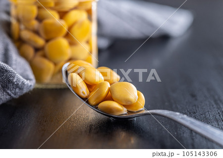 Lupini beans in brine. Pickled lupin in spoon on black table. 105143306