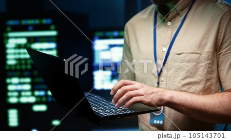 Precise mechaninc doing routine system scan, typing data on laptop of needed repairs in blade servers housing advanced data storage equipment supporting important IT workloads 105143701