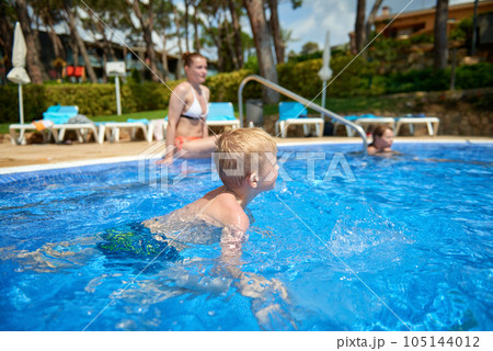 Young boy kid child eight years old splashing in swimming pool having fun leisure activity. Boy happy swimming in a pool. Activities on the pool, children swimming and playing in water, happiness and Young boy kid child eight years old splashing in swimming pool having fun leisure activity. Boy happy swimming in a pool. Activities on the pool, children swimming and playing in water, happiness and 105144012