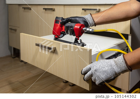 Worker repair wooden drawer of cabinet with pneumatic nail gun. Worker repair wooden drawer of cabinet with pneumatic nail gun. 105144302