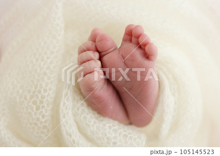 The tiny foot of a newborn baby. Soft feet of a new born in a white wool blanket. Close up of toes, heels and feet of a newborn. Knitted white heart in the legs of a baby. Macro photography. 105145523
