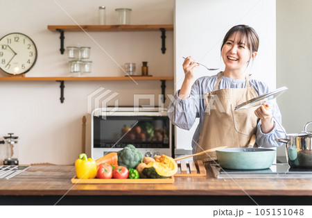 キッチンで料理の味見をするエプロン姿の女性・主婦（カフェ） 105151048