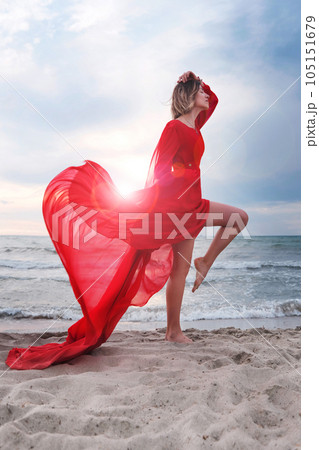Woman wearing red flying dress on a beach. Female energy  105151679
