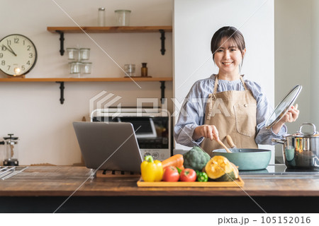パソコンでレシピ動画を見ながら料理をする女性 パソコンでレシピ動画を見ながら料理をする女性 105152016