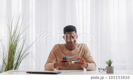 Online shopping. Internet payment. Phone banking. Cheerful man buying purchase on mobile cell application with credit card money transfer at home. 105153810