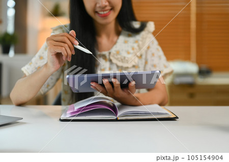 Cropped shot of young woman sitting in home office and using digital tablet. Technology, freelance work and lifestyle concept 105154904