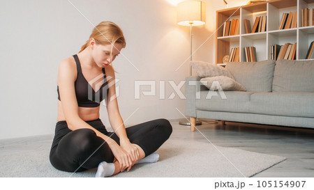 Exhausting fitness. Boring fitness. Sport motivation. Tired upset sad depressed girl sitting cross-legged on floor at light home interior with free space. 105154907