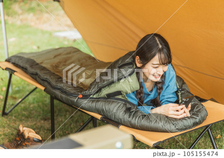 キャンプ場で寝袋・シェラフで寝ながら本を読む若い女性キャンパー（読書） 105155474