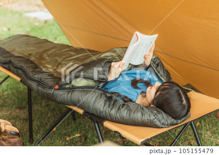 キャンプ場で寝袋・シェラフで寝ながら本を読む若い女性キャンパー（読書） 105155479