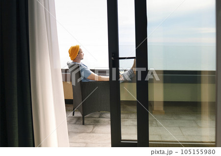 Young man in gray casual clothes and yellow hat sits on wicker chair and holds glass of champagne. 105155980