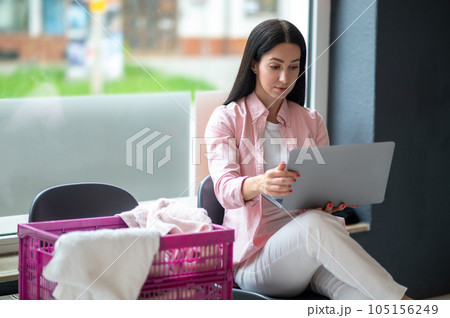 Woman with laptop at laundromat doing job project, connection and multitask, working on computer while washing clothes. 105156249
