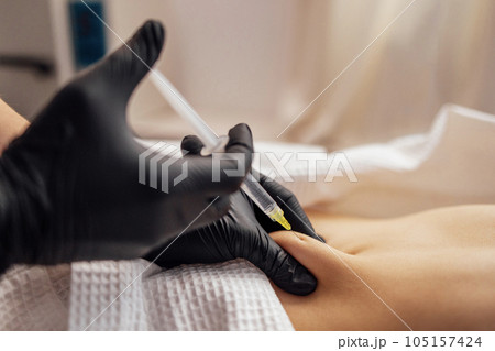 Close up of hands in black gloves of cosmetologist giving injection into stomach of client. 105157424