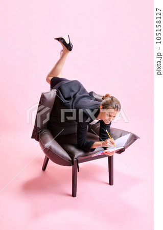 Anger and irritation. Business Woman lying on armchair in weird pose and putting notes on against pink studio background Anger and irritation. Business Woman lying on armchair in weird pose and putting notes on against pink studio background 105158127