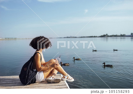 Beautiful mixed race female teenager sits on wooden pier Beautiful mixed race female teenager sits on wooden pier 105158293