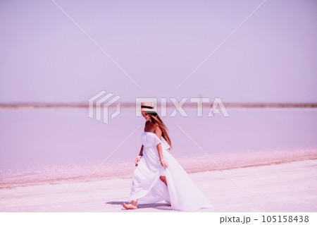 Woman in pink salt lake. She in a white dress and hat enjoys the scenic view of a pink salt lake as she walks along the white, salty shore, creating a lasting memory. Woman in pink salt lake. She in a white dress and hat enjoys the scenic view of a pink salt lake as she walks along the white, salty shore, creating a lasting memory. 105158438