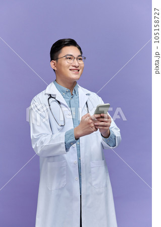 Cheerful man doctor holding mobile phone over purple studio background 105158727